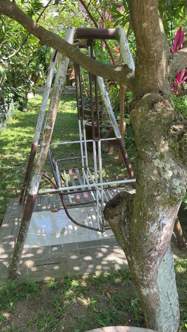 Altalena da giardino in metallo vuota che dondola dolcemente in un cortile soleggiato