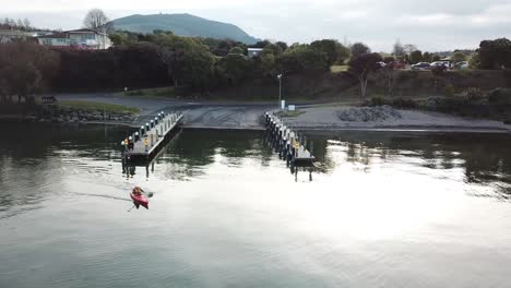 aerial view, a man kayaking out to the lake from a jetty, in the early springtime on a calm day in new zealand, pan slowly