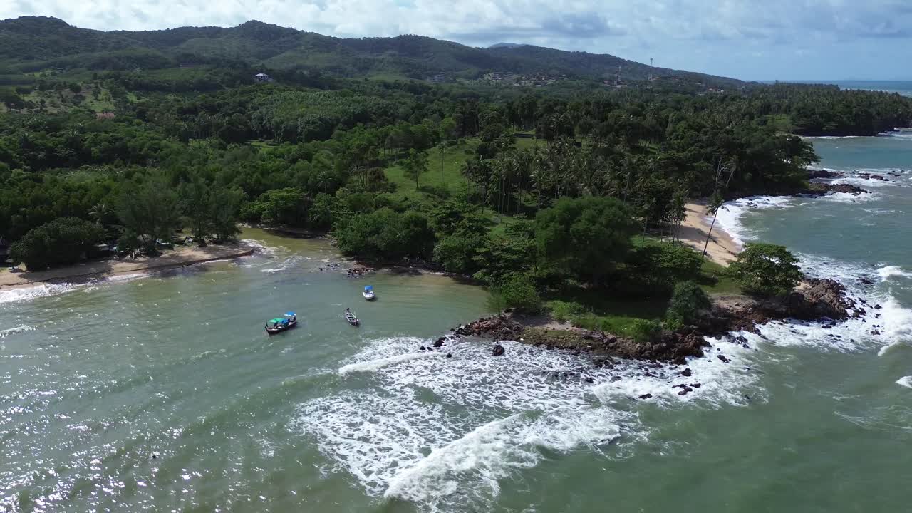 Aerial drone Aerial drone footage of Koh Lanta, Thailand, featuring traditional longtail boats anchored near a tropical coastline with palm trees, rocky shore and remote beaches in the background