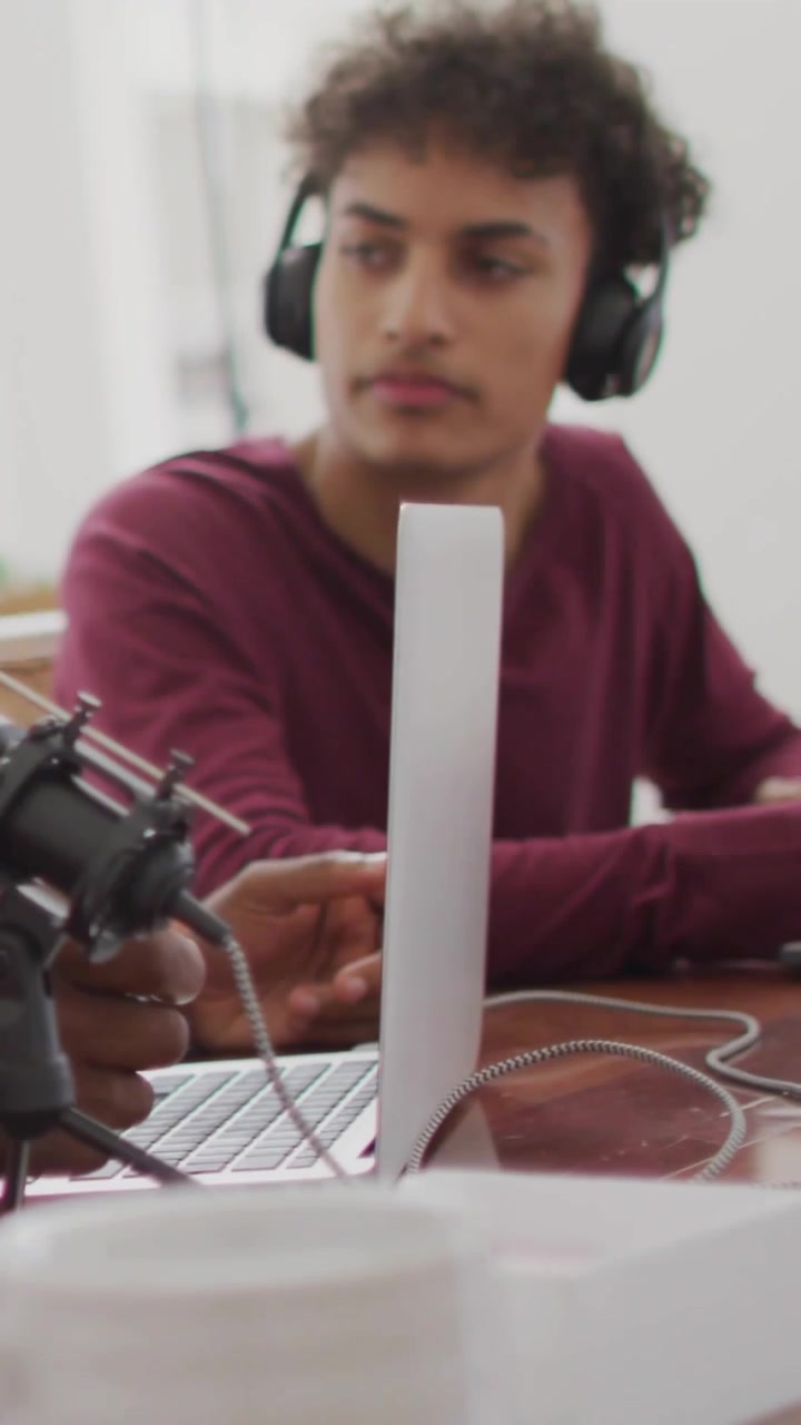 Video vertical: HUD emergente mientras un hombre con auriculares usa un micrófono y una laptop, con gráficos que cambian para podcasting.