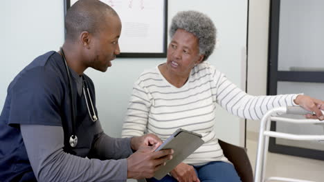 Médico-Afroamericano-Usando-Tableta-Y-Hablando-Con-Una-Mujer-Mayor-En-El-Hospital,-Cámara-Lenta