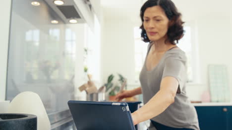 mujer madura en la cocina en casa cocinando una comida siguiendo la receta en una tableta digital