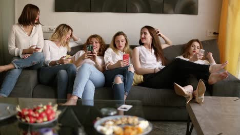 Six-beautiful-girls-relaxing-on-the-couch.-Girls-are-looking-into-their-mobile-phone.-Have-a-rest.-Hen-party-concept.-Identical-clothes.-Chatting