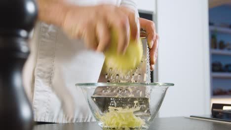 hand of chef grating potatoes in glass bowl. close up