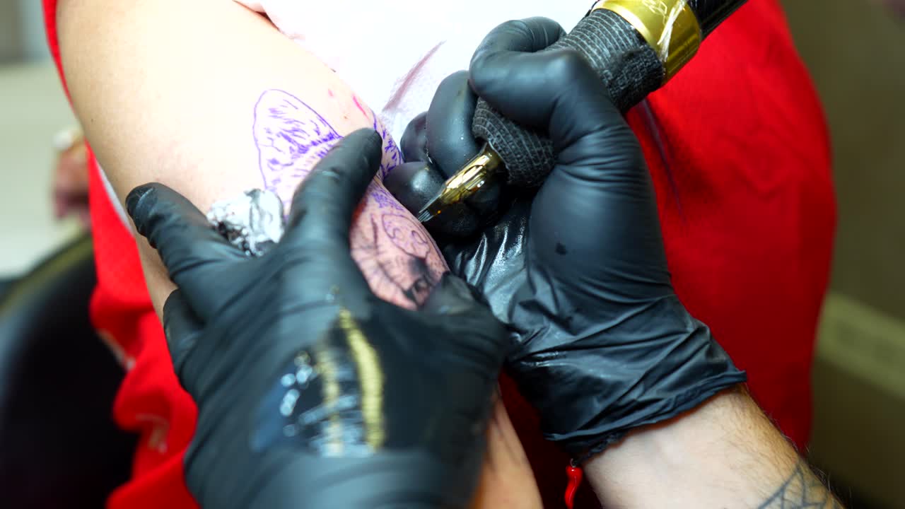 Artist tattooing portrait of client's dog on upper arm. Focused closeup shot