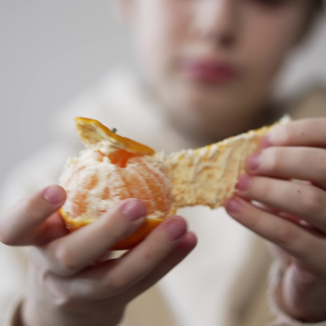 Teenager's hands in focus peeling the fruit. Unrecognized boy holding tangerine and taking off its peel slowly. Close up. Blurred backdrop