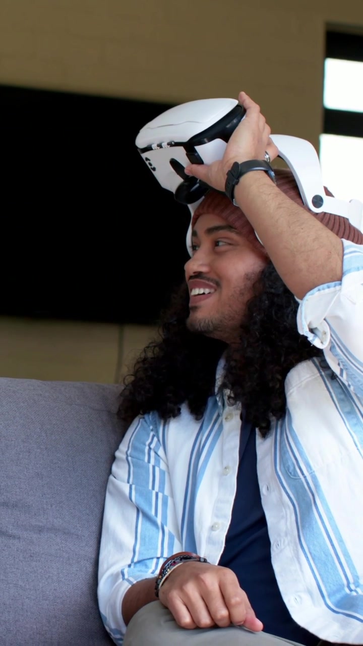 Vertical video: Holding white VR headset, man lowering it over eyes on couch, testing fit