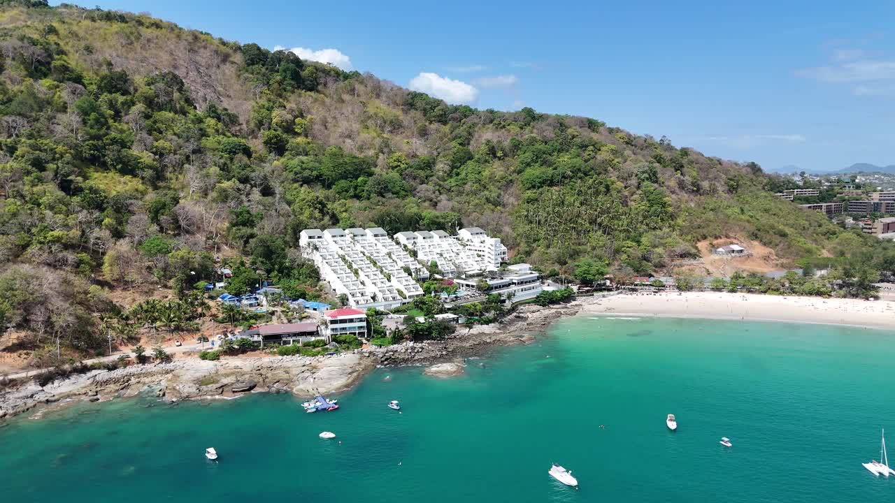 드론 영상은 태국 푸켓의 조용한 해안선을 포착합니다. 푸른 초록색, 푸른 물, 그리고 은 하늘 아래 고정된 배를 보여줍니다.