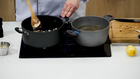 a chef stirs chicken in a pot on the stovetop, while another pot beside it boils water for pasta. fresh ingredients and utensils are visible on the kitchen counter