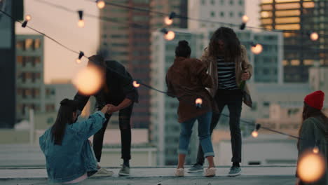 happy group of friends on rooftop with arms raised celebrating friendship enjoying hanging out together drinking alcohol embracing freedom looking at urban city skyline at sunset