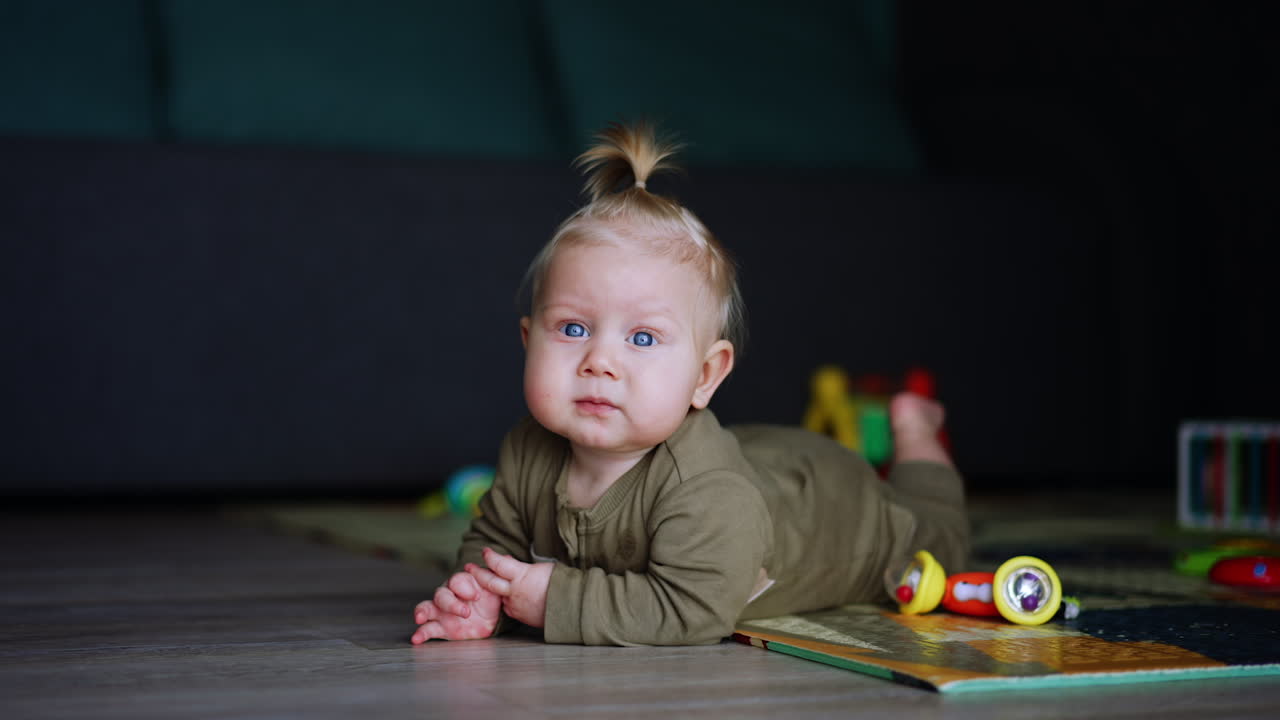 Kleines Baby im Strampler liegt drinnen auf dem Boden. Blondes Kind versucht auf dem Boden zu krabbeln und weint.