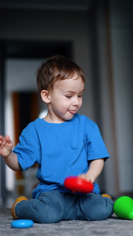 baby boy plays with the details of toy pyramid. kid rolls the ring by the floor and follows it. vertical video.