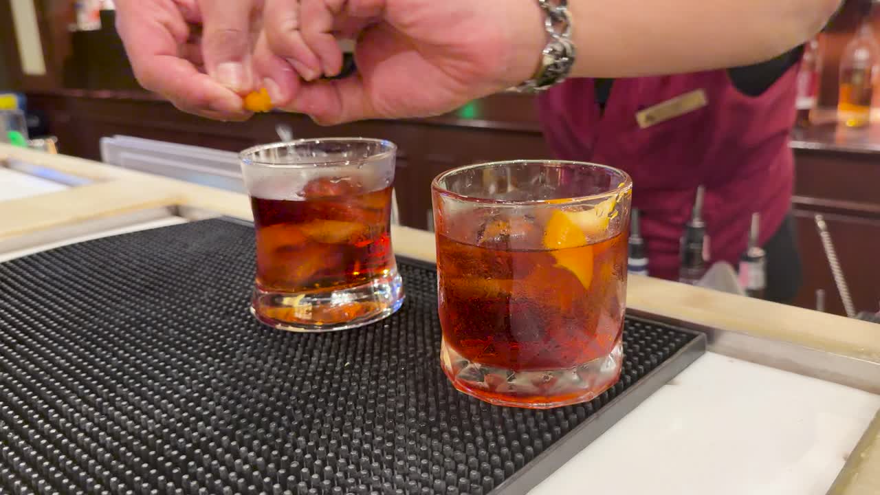 Bartender twists citrus peel over cocktails in warm bar lighting, close-up, slow motion effect