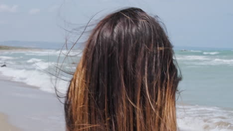 Vista-Trasera-De-Una-Mujer-Con-Cabello-Castaño-Caminando-Por-La-Orilla-Del-Mar-En-La-Brisa-De-Verano