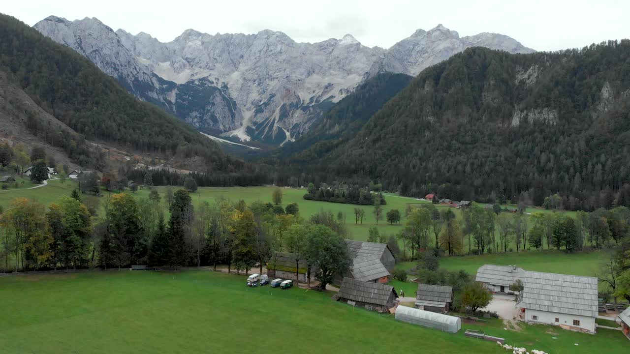 Drone flying towards a village with campervan parked in a eco farm and massive mountains in the background. Jezesko Valley in Slovenia in Autumn season aerial view