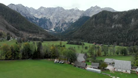 drone flying towards a village with campervan parked in a eco farm and massive mountains in the background. jezesko valley in slovenia in autumn season aerial view