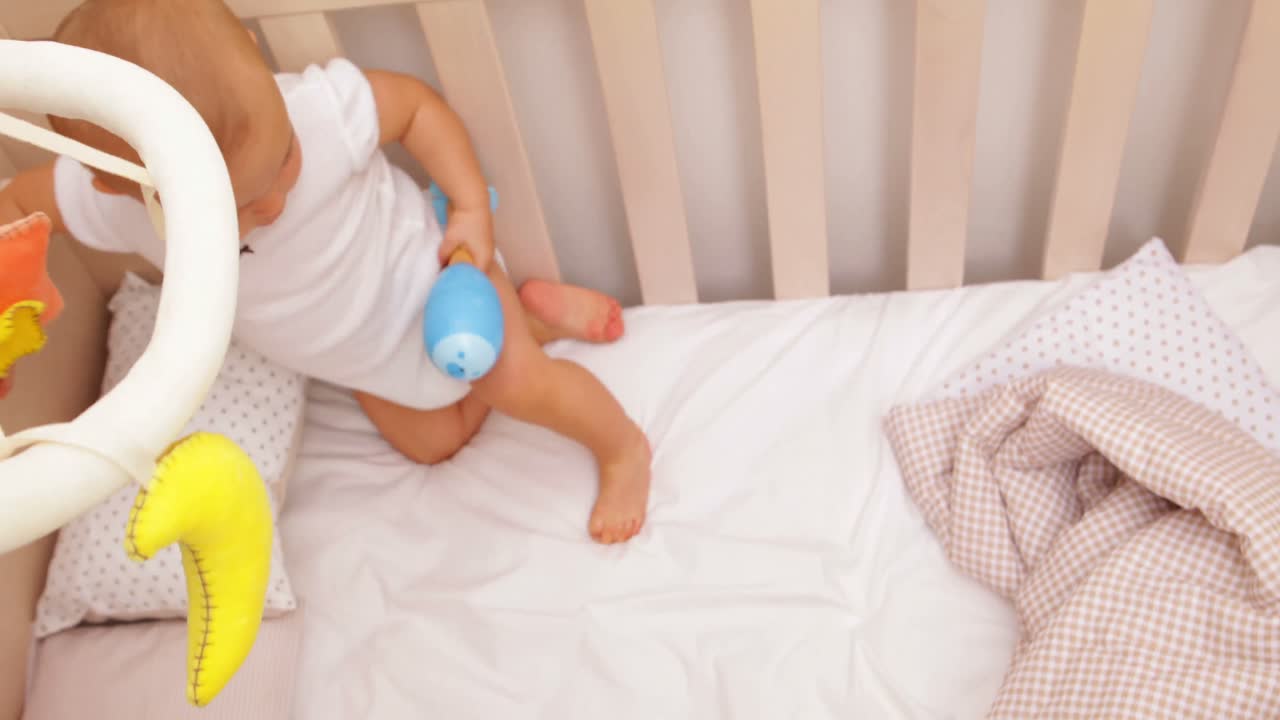 Bambina carina che si alza nella sua culla giocando con la giostrina.