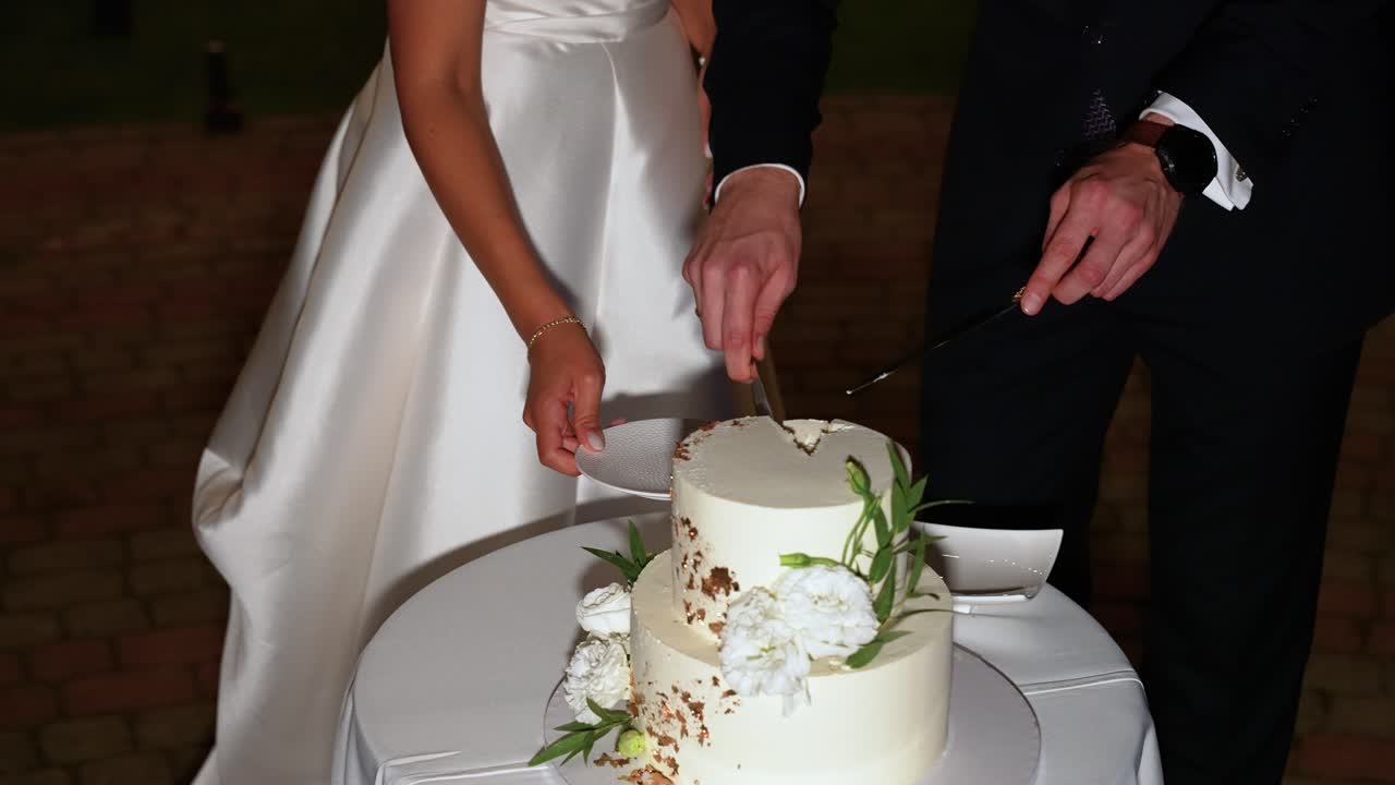 Uma noiva e um noivo fatiam elegantemente o bolo de casamento. O bolo lindamente decorado apresenta detalhes florais, capturado com iluminação suave e quente. Um momento de amor e celebração.