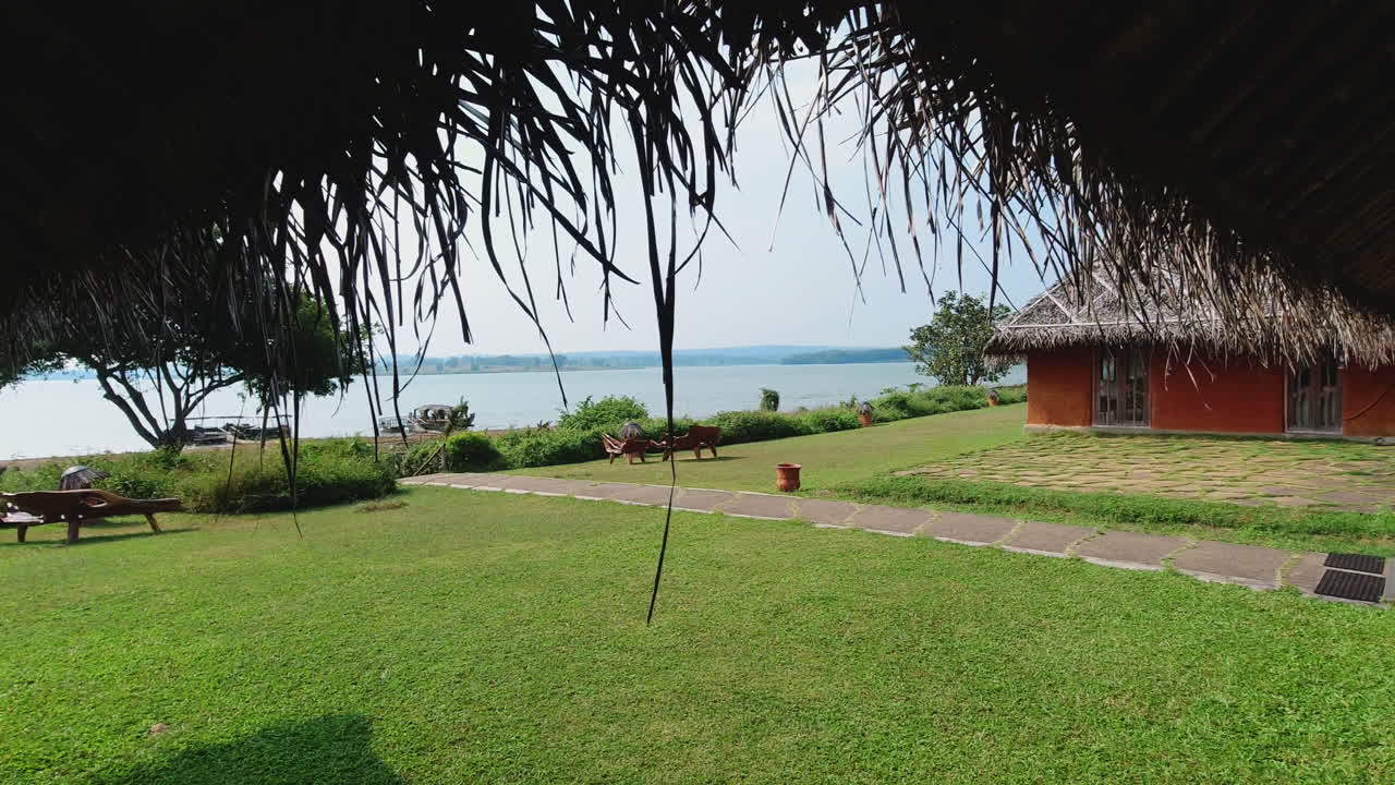 Peaceful distant view of Kabini river water from a riverside resort with a thatched hut during a hot day afternoon in Karnataka, India. Slow motion.
