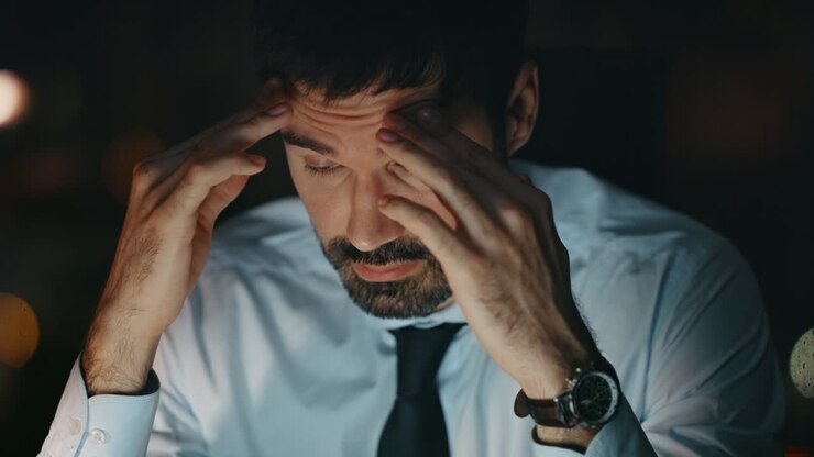 Primo piano di un CEO sovraccarico con mal di testa, seduto in ufficio a tarda sera. Uomo in burnout.