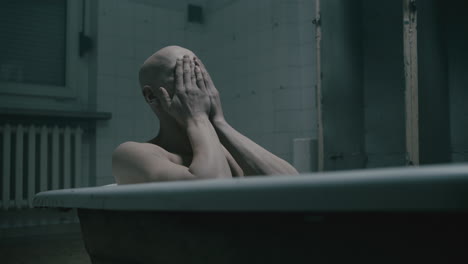 pale bald skinny man takes a bath in the creepy old bathroom at night