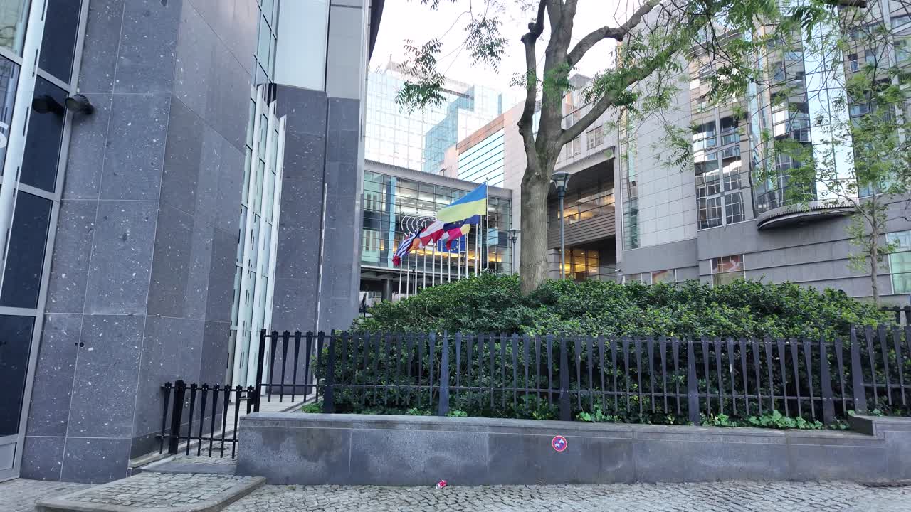 Distant view of EU Parliament with flags behind trees and fencing