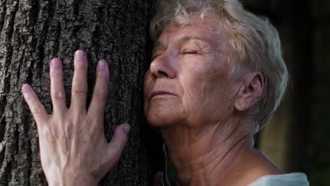 Mujer-Mayor-Tranquila-Haciendo-Ejercicio-De-Respiración-Junto-Al-árbol-En-El-Parque