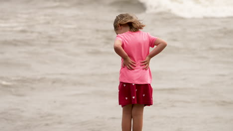 Ein-Kleines-Mädchen-Dreht-Sich-Um-Und-Rennt,-Als-Wellen-An-Einem-Meeresstrand-Auf-Sie-Spritzen