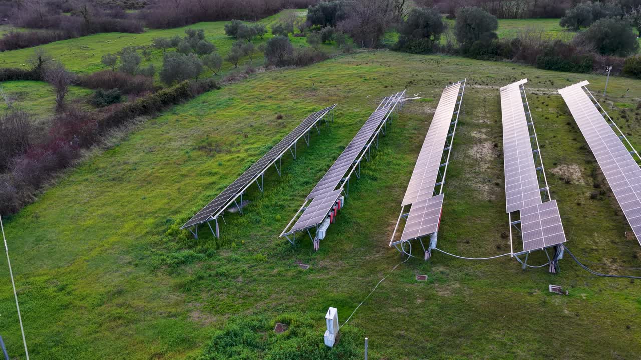 Luftfoto af lille solcellepark med paneler på grøn mark i landlige omgivelser, der leverer vedvarende grøn energi og bæredygtig elproduktion