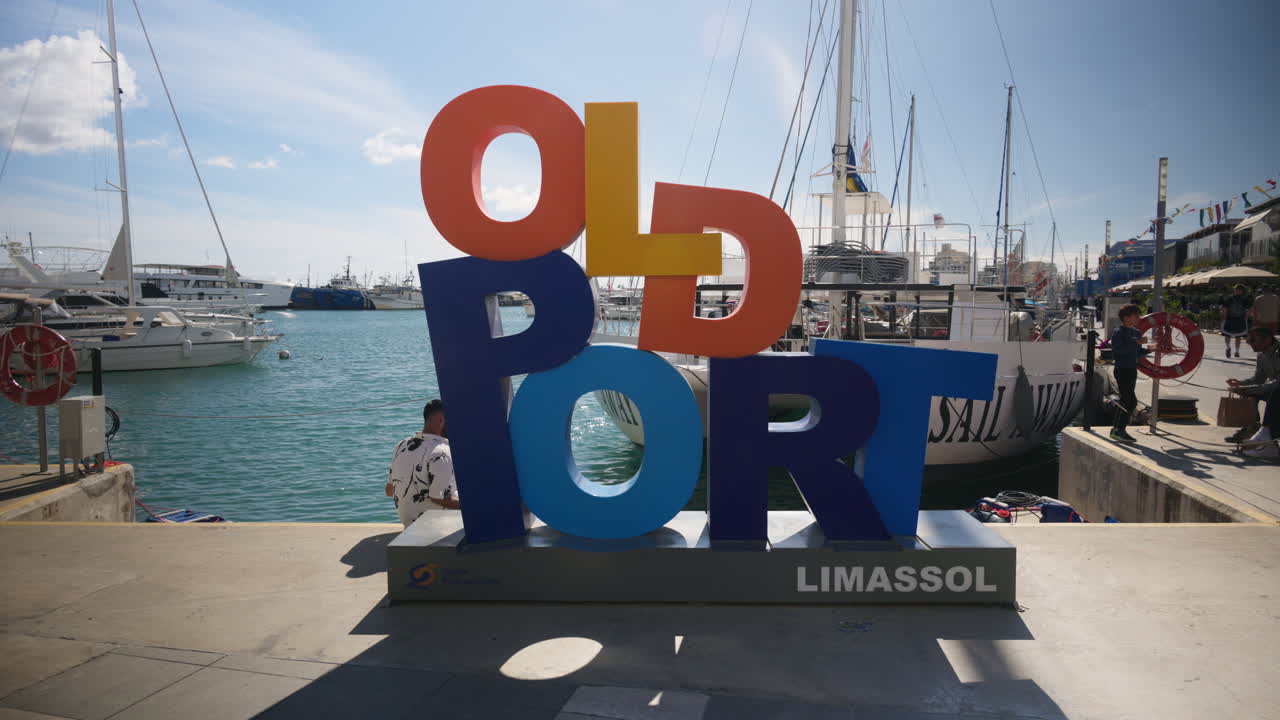 Limassol, Cipro - 26 febbraio 2026: Insegna luminosa e colorata "Old Port Limassol" situata vicino al porto turistico con yacht e barche sullo sfondo