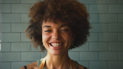 portrait of laughing female owner or member of staff wearing apron inside shop or cafe