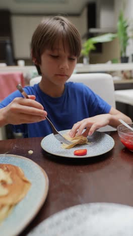 boy eating pancakes and strawberries for breakfast