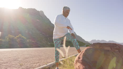 Happy-senior-biracial-woman-stretching-in-mountains-on-sunny-day,-in-slow-motion