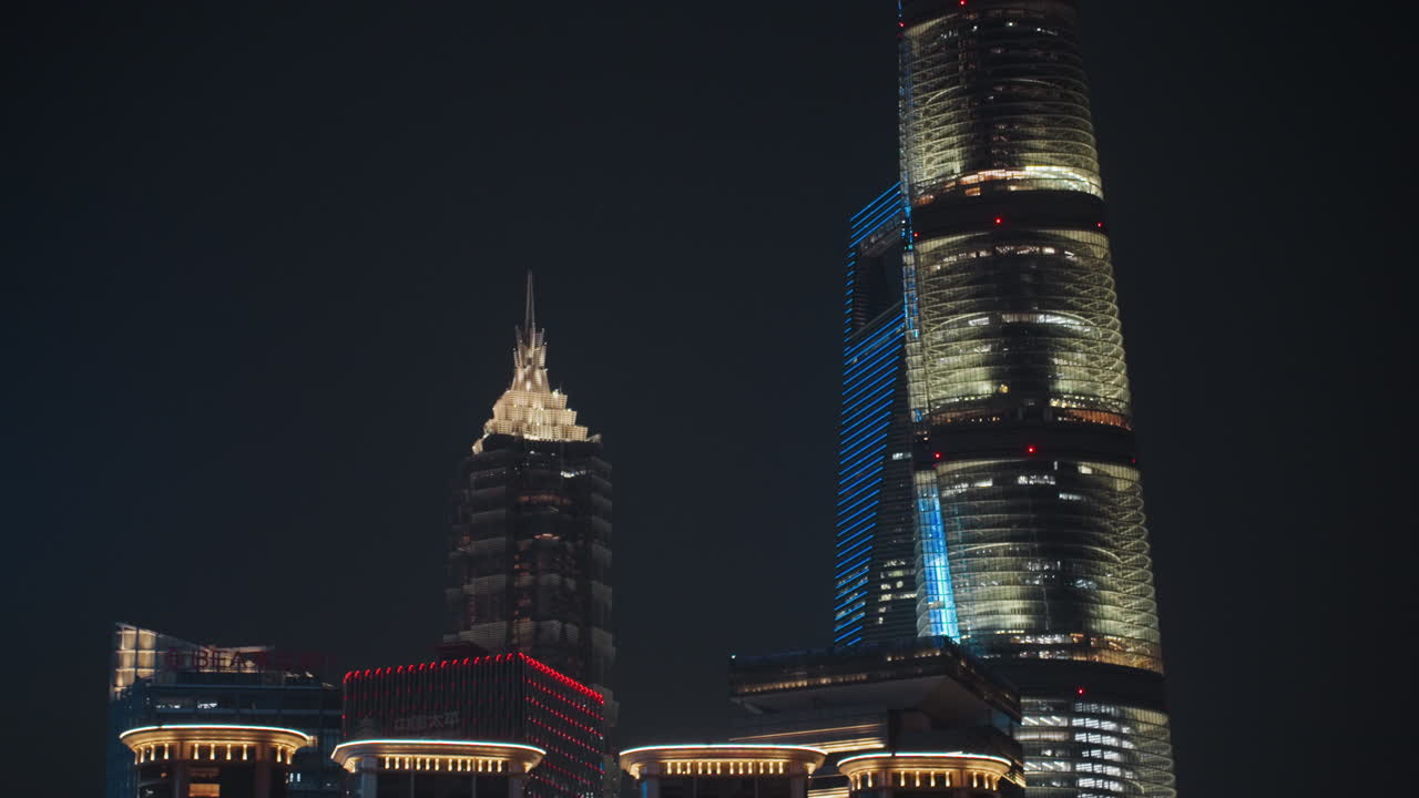 Torre de vidro em espiral à noite, luzes em fita traçando a fachada curva, reflexo na orla e brilho do distrito corporativo, atmosfera noturna calma, inclinação aérea revelando a silhueta de um marco moderno