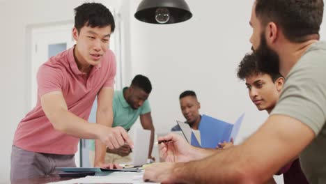 happy diverse male friends talking and using laptop in living room