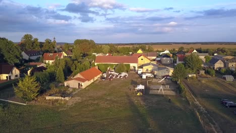 Dramatischer-Drohnenflug-Aus-Der-Luft,-Der-Langsam-Nach-Unten-Sinkt.-Drohnenaufnahme-Eines-Bauernhofs-Bei-Sommerlichem-Sonnenuntergang-Mit-Langen-Schatten-Auf-Einem-See-In-Einem-Kleinen-Dorf-In-Brandenburg,-Deutschland