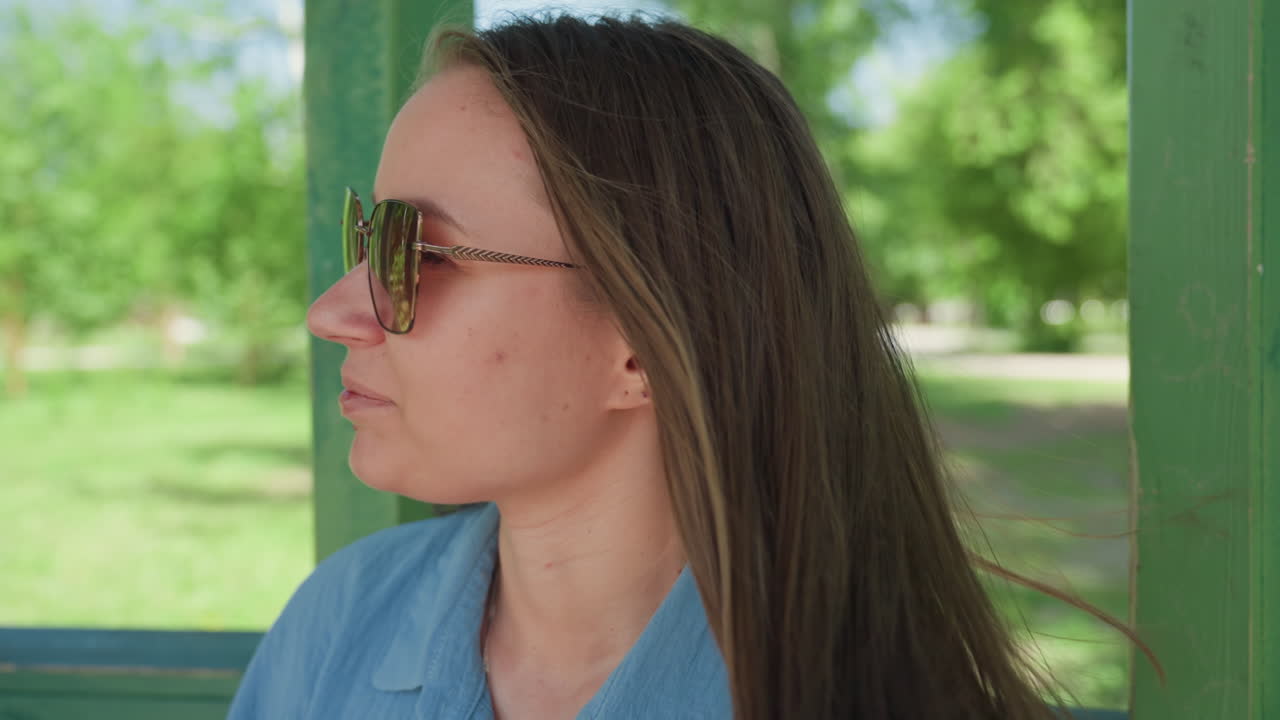 Mujer serena contemplando un paisaje pintoresco, mujer equilibrada con gafas de sol admirando un entorno tranquilo al aire libre, mujer calmada y serena disfrutando de un momento de paz en un parque