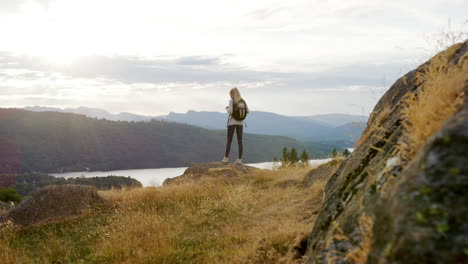 una mujer caucásica joven adulta de pie en un pico admirando la vista durante una caminata por la montaña, vista de atrás