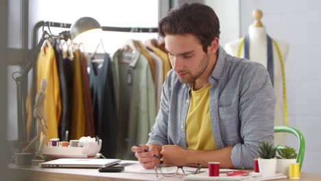 male owner of fashion business working on designs receives message on mobile phone sitting at desk