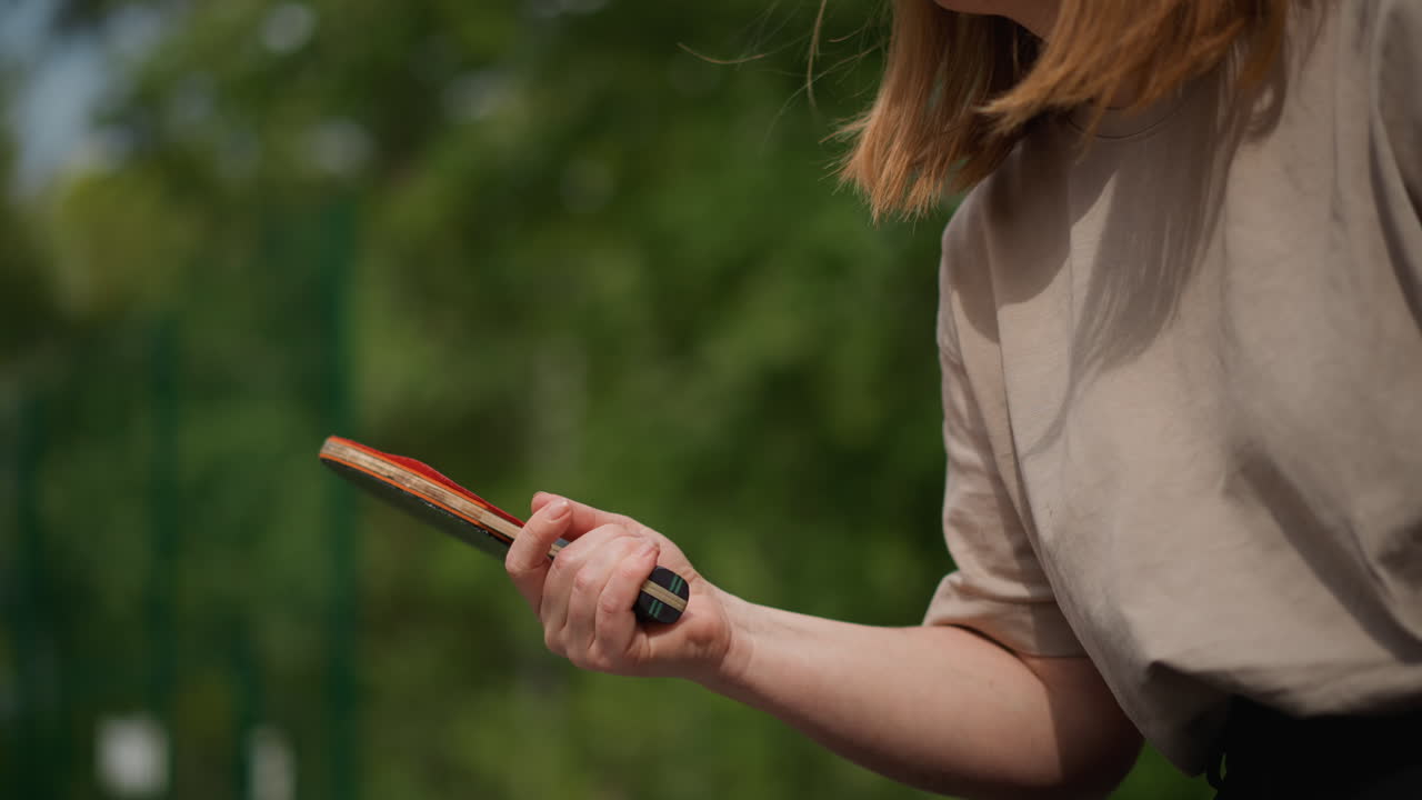 Teenagepige forbereder sig til bordtenniskamp, ung kvinde fokuserer på teknikken med bat udendørs, ung kvinde øver sig flittigt på sit ketchergreb i et udendørs bordtennisområde
