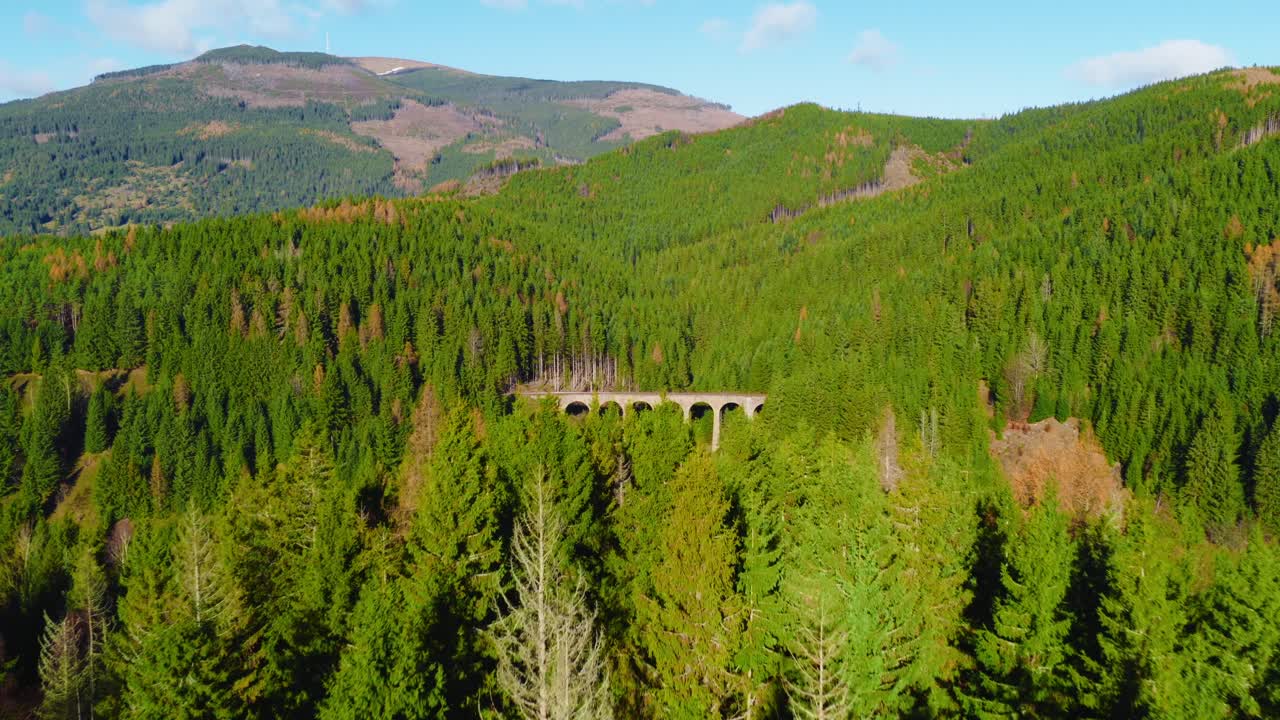Drone view of the historic Telgárt viaduct in Slovakia, surrounded by dense green forest and rolling mountain slopes in bright daylight