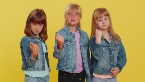 three young girls in denim jackets pose together against a yellow background