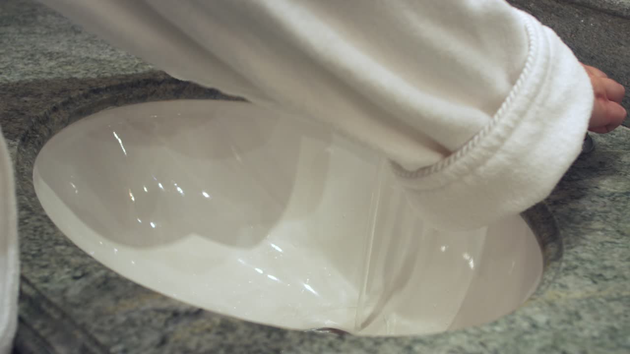 ⁇ 색 욕조 를 입은 여자 가 물  ⁇  을 돌리고 손 을  ⁇ 고 있다