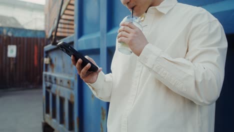 man using smartphone while drinking a beverage outside