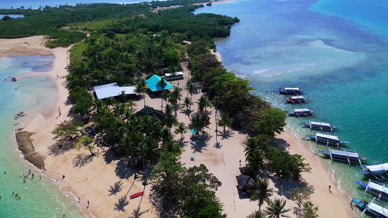 Vista aerea di Palawan, destinazione turistica di punta, l'isola di Cowrie, con imbarcazioni tradizionali filippine e strutture del resort, ripresa da drone sopra acque turchesi vibranti e una spiaggia di sabbia bianca.