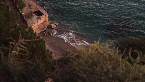 Hidden-beach-through-bushes-at-sunset,-waves-washing-sand