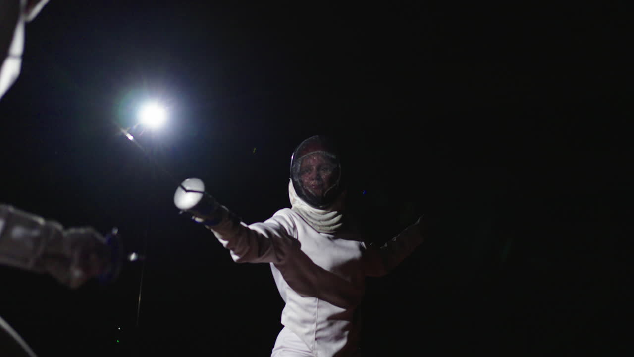 A female fencer in action under a spotlight at night