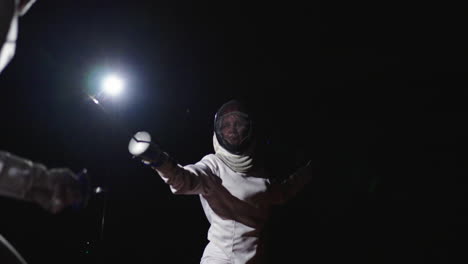 a female fencer in action under a spotlight at night