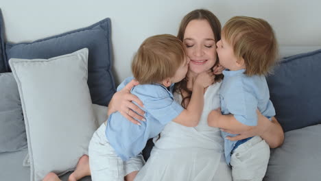 Mama-Sitzt-Mit-Einem-Laptop-Auf-Der-Couch.-Zwei-Jungenkinder-Singen-Und-Küssen-Ihre-Mutter.-Glückliche-Familie,-Liebevolle-Kinder