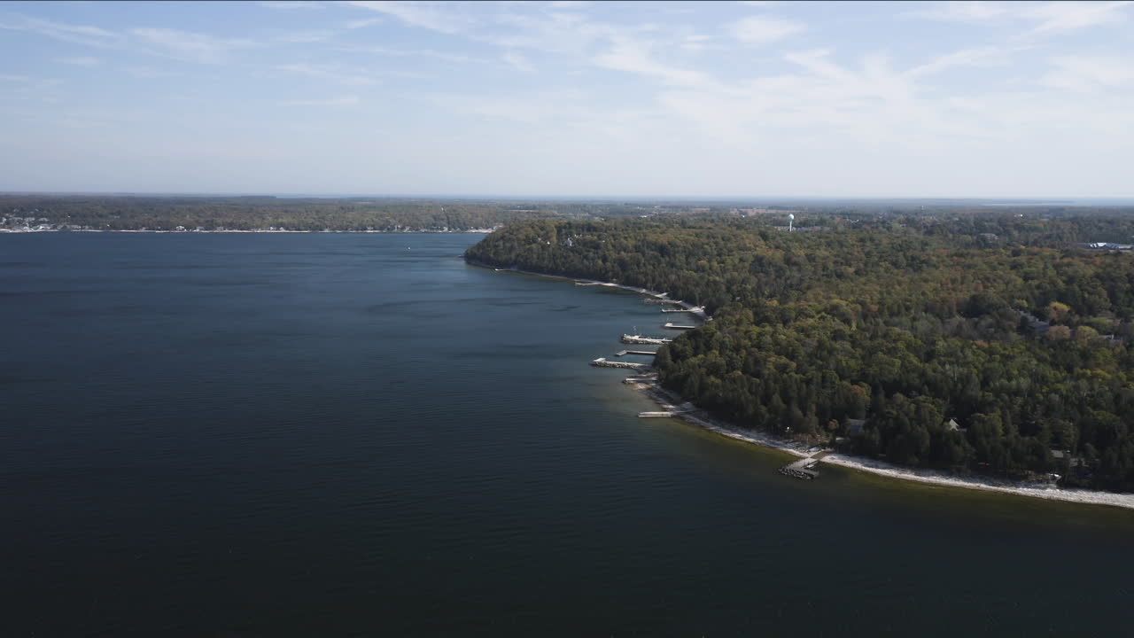 Hamparan luas air danau biru tua melengkung mengelilingi semenanjung berhutan di Door County, tempat hutan hijau bertemu garis pantai dalam harmoni yang tenang di bawah langit terbuka yang cerah